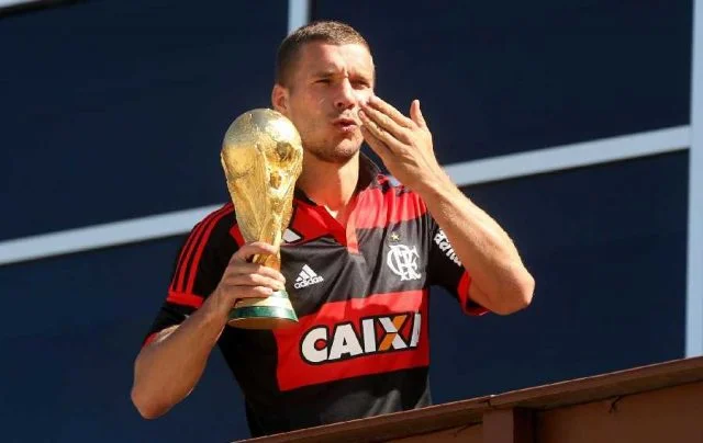 Vestindo o uniforme do Flamengo, Lukas Podolski manda beijo, com a Taça da Copa Mundo